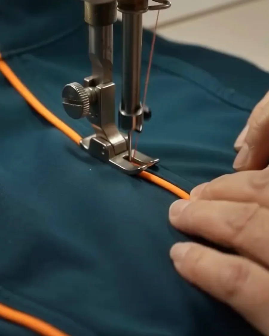 Sewing machine stitching orange piping onto a teal jacket